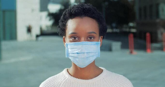 Portrait Of African American Sick Infectious Female Patient In Medical Protective Mask Stands Alone Isolated Looks At Camera Crosses Arms In Front Of Her Shows Prohibition Stop Sign Puts Restrictions