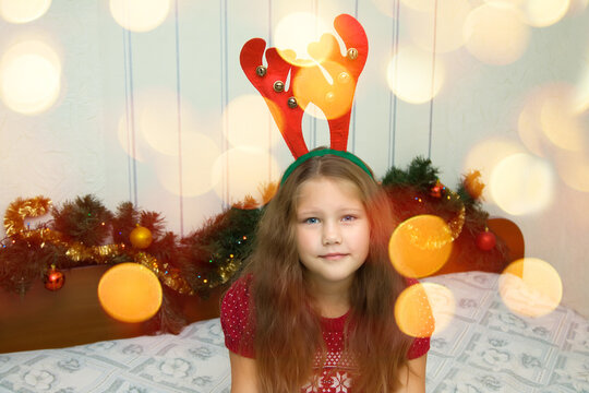 Beautiful happy 7 year old girl wearing cute red christmas hair band with reindear antlers
