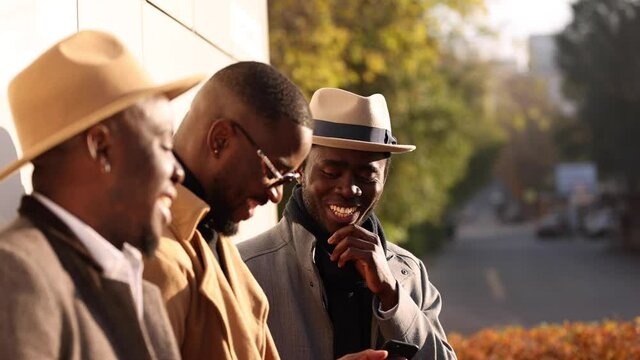 Stylish African friends using their smartphones together in an autumn city