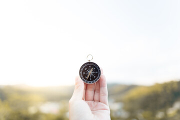 Hand holding a compass pointing to the north, with blurred mountains in the background