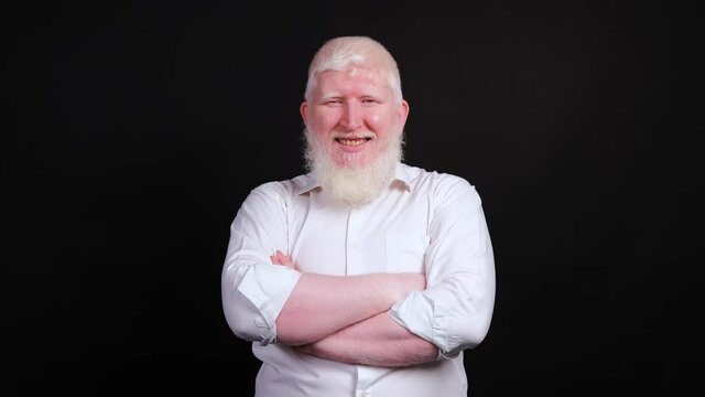 Albino man in white shirt doing thumb up gesture, looking at camera with a smile, isolated on black background.