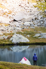 The tourist is standing near the tent. Lake in the Carpathian mountains. Girl in a warm jacket.