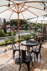 restaurant terrace with a table, chairs and umbrellas, in the background a city street with plants, modern style