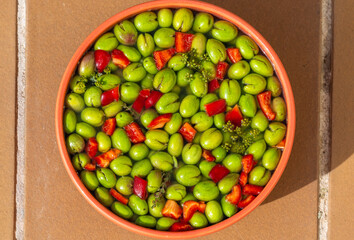 Bowl of freshly picked green olives seasoned with red pepper, fennel, garlic and thyme on a tile