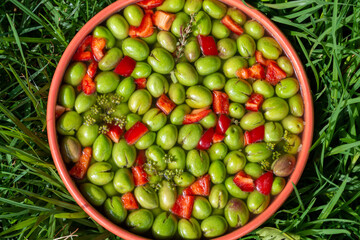 Bowl of freshly picked green olives seasoned with red pepper, fennel, garlic and thyme on a green grass background