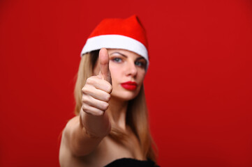 A young woman in a Santa hat smiles and shows off her thumb. The concept for the new year and Christmas.