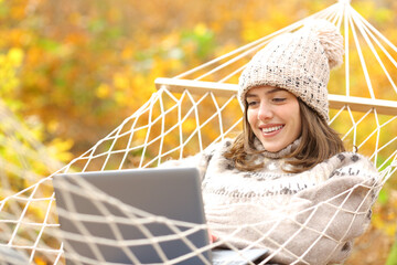 Happy woman on hammock using laptop in autumn