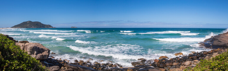 Fototapeta na wymiar Mar azul batendo nas pedras de uma Praia tropical do Brasil, ilha de Florianópolis, Praia do Santinho, Florianopolis, Santa Catarina