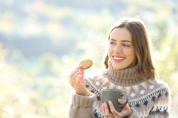Happy woman eating cookie and drinking coffee in winter