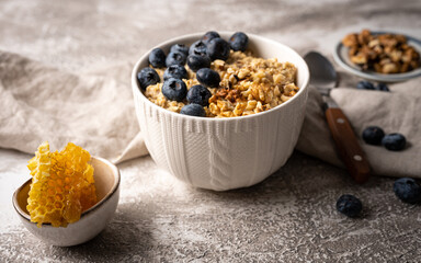 Healthy breakfast bowl: oatmeal with blueberries, nuts and honeycomb piece.