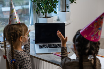 Young girls wearing a face mask during the Covid-19 or coronavirus pandemic on birthday sitting at...
