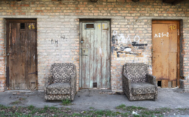 Two old brown vintage old armchairs stand near an abandoned brick building