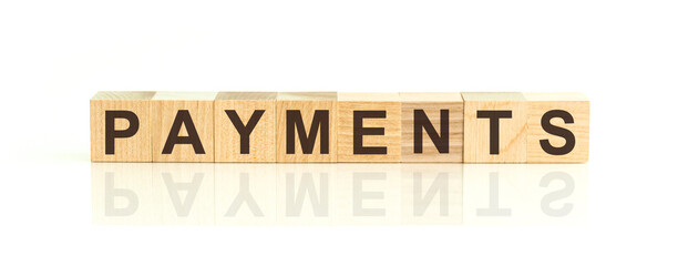 Wooden Blocks with the text: payments. The text is written in black letters and is reflected in the mirror surface of the table.