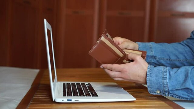 Jobless man looking at his empty wallet in front of the computer.