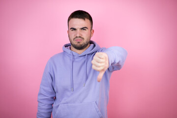 Young handsome man wearing casual sweatshirt over isolated pink background with angry face, negative sign showing dislike with thumb down