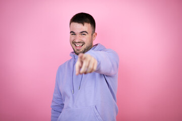 Young handsome man wearing casual sweatshirt over isolated pink background laughing at you, pointing finger to the camera with hand over body, shame expression