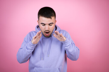 Young handsome man wearing casual sweatshirt over isolated pink background shouting and screaming loud down with hands on mouth