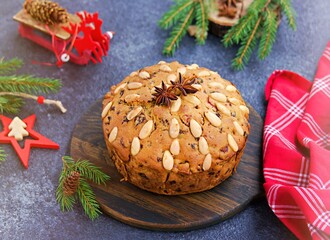 A traditional Scottish Christmas fruit Dundee cake with a mix of dried fruits, decorated with peeled almonds on a wooden board on  a dark concrete background.