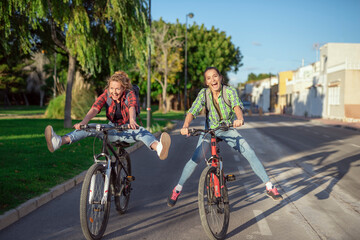 Obraz premium Two pretty young caucasian girls having fun on bicycles along the street. Best friends enjoying a day on bikes. Sunny summer evening