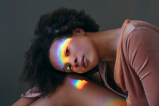 Woman resting head on knees with rainbow across face