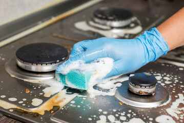 Female hand cleaning gas stove using sponge and detergents. Cleaning a gas stove with kitchen...
