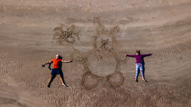 drone selfie of a young couple on the sand laying with a drawn rabbit