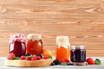Fototapeta na wymiar Sweet jam in glass jars with ripe berries on brown wooden table