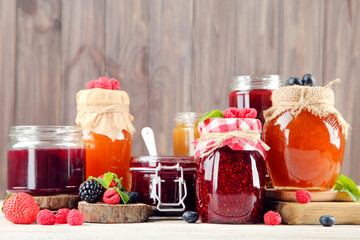 Fototapeta na wymiar Jam in glass jars with fresh berries on wooden background
