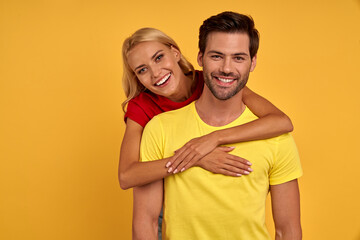 Smiling young couple friends in colored t-shirts posing isolated on yellow wall background studio portrait. People emotions lifestyle concept. Mock up copy space. Hugging