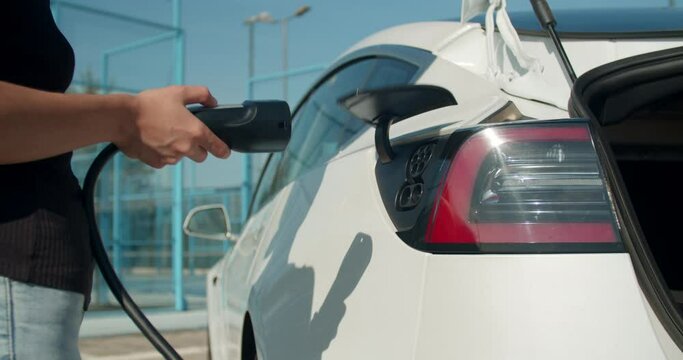 Female hand plugs in a charging cable in an electric car.