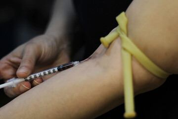 Lateral view of the arm of a cocaine addict, as she inserts the syringe needle into her arm, to...