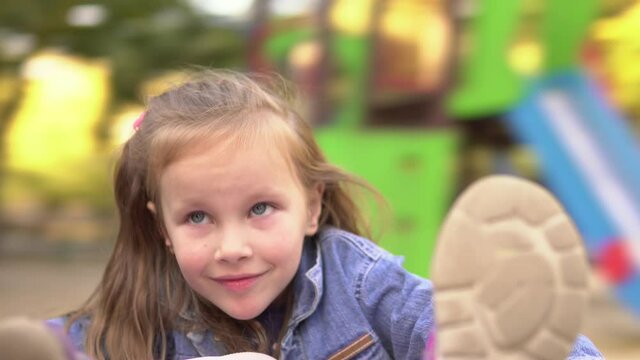Little beautiful girl is spinning on the carousel looking at the camera and smiling happily.Playground.4k