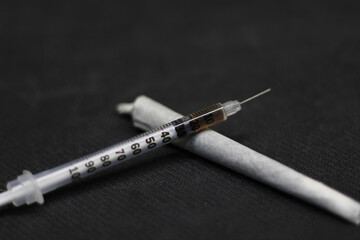 Front and close view of a syringe full of cocaine, resting on a cane of ganja and cocaine, both...