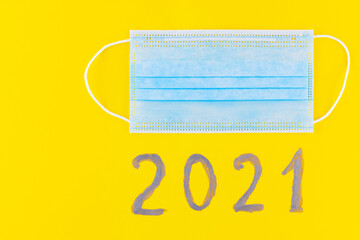 Text 2021 on a yellow background and surgical mask. Concept of the New Year with blue protective mask. Celebrating New Year in quarantine, covid-19, coronavirus. Top view