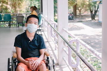 Asian special child on wheelchair wearing a protection mask against PM 2.5 air pollution and flu Covid 19 or Coronavirus on public path background, N95 to prevent the spread of the virus disease 2020.