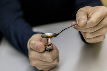 Close-up view of a drug addict holding a teaspoon and a lighter in his hand while cooking cocaine so that he can inject it into a vein with a syringe.