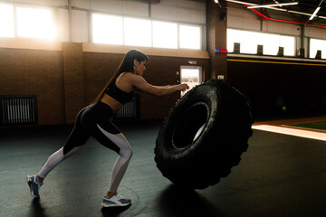 Caucasian strong athlete woman working out with heavy tire indoors