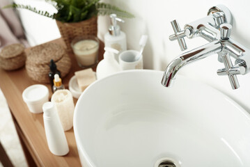 A light-colored sink with a tap next to the tubes of cream, skin care cosmetics, and face serums. The concept of taking care of the skin in the morning in the bathroom. Nobody
