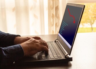 man in blue shirt working from laptop computer viewing finance and economic crisis graph