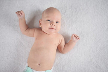 Cute emotional smiling funny newborn boy laying on bed top view. Baby facial expressions.