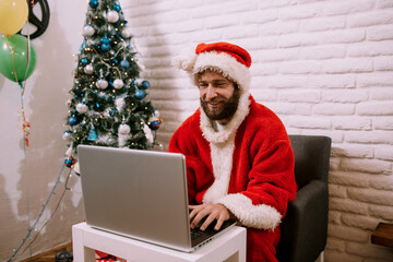 Christmas online congratulations from Santa. Santa Claus using notebook laptop for distance Christmas call kids sitting near Christmas tree at home. Happy New Year Covid 2021