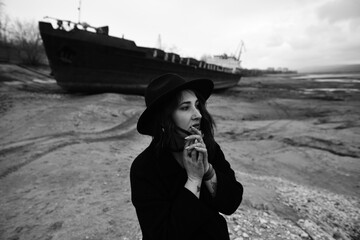 Black and white portraits of a young woman against large sea vessel on the dry riverbed