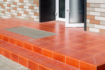 threshold with a paved red tile and a foot mat at the open front door of a brick walled building on...