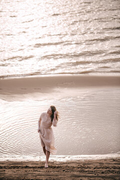Beautiful woman in an exquisite dress walks barefooted in a river at sunset time