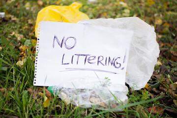 Close up "no littering" sign near stack of garbage. Plastic waste. Pollution of parks by used rubbish. Ecology activism 
