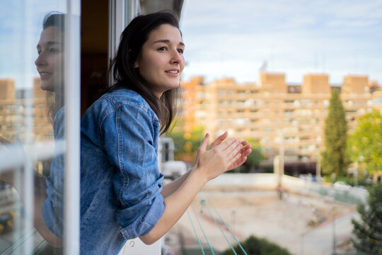 Young Woman Applauding From The Window During Coronavirus Lockdown.