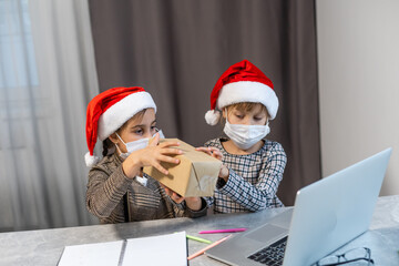 Christmas greetings online. two little girls in medical masks a laptop. Shows gifts, online purchases to the camera. Greeting video calls to friends, relatives and parents