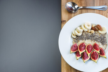 a bowl with breakfast oatmeal porridge with superfood chia seeds, fresh figs and banana on a wooden board on grey background , served with black tea