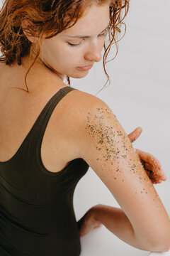 Woman using body scrub on white background.