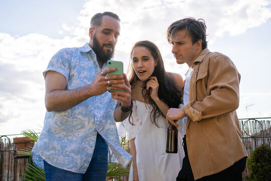 Three Friends Checking A Cellphone Outdoors.